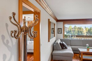 A modern living room with a grey sofa, a wooden coffee table, and a view of a mountainous landscape through large windows. - Stunning apartment with private parking and a balcony (Crans-Montana)