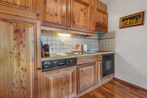 A kitchen with wooden cabinets, a dishwasher, an oven, and a tiled backsplash. - Stunning apartment with private parking and a balcony (Crans-Montana)