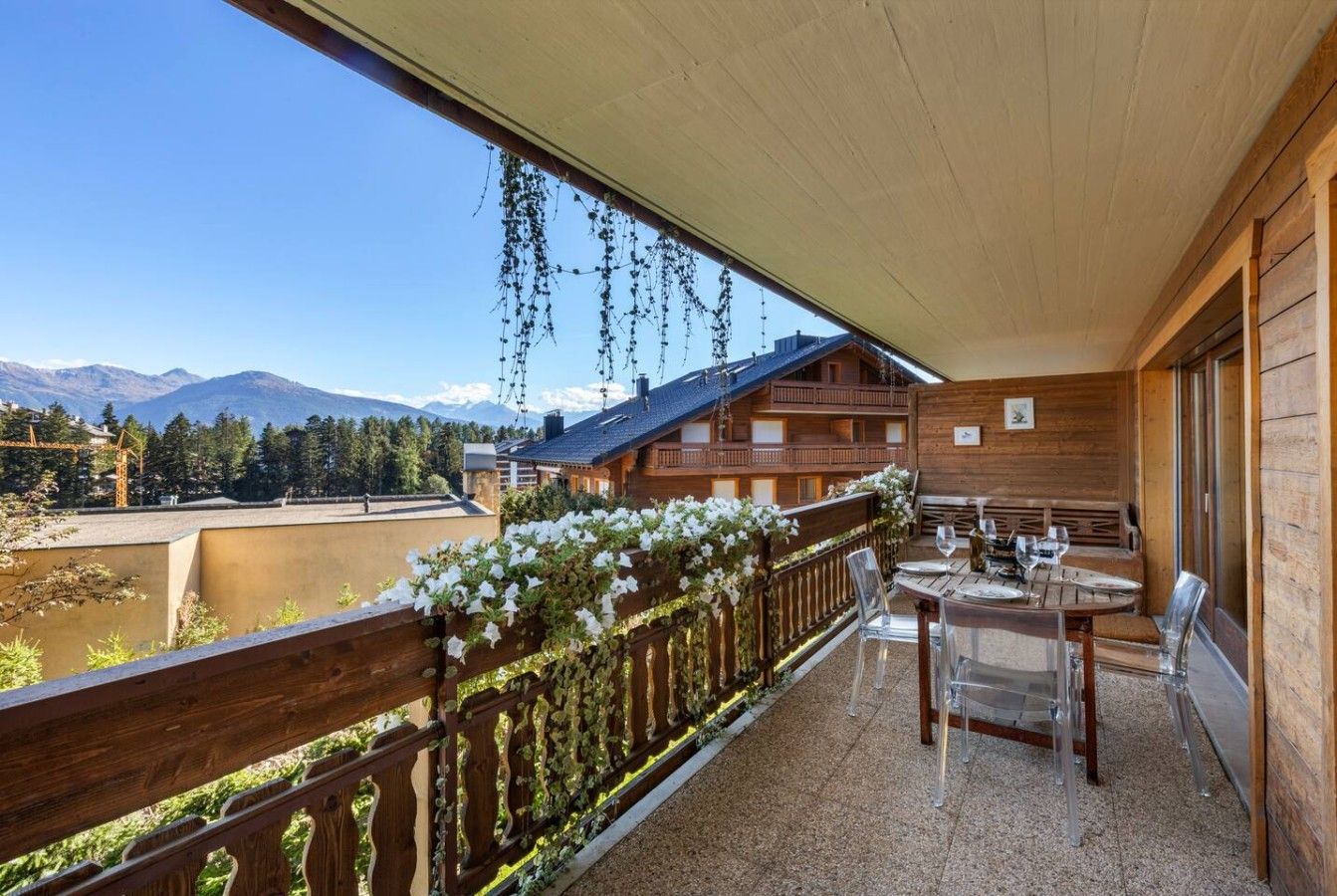 Ein Holzbalkon mit Tisch und Stühlen, mit Blick auf eine Berglandschaft.