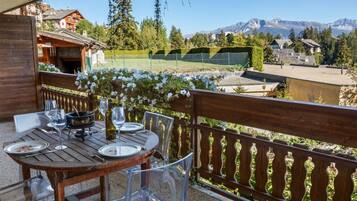 An outdoor dining area with a wooden table and chairs, a wine bottle, and a view of mountains in the background.