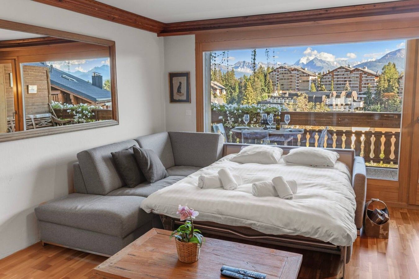 Une pièce comprenant un lit, un canapé, une table basse en bois et offrant une vue sur les montagnes et les bâtiments.
