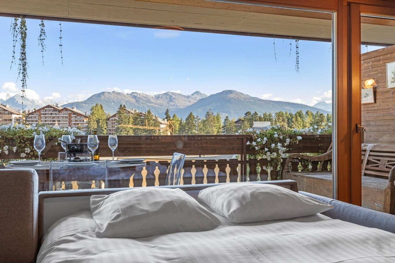 Ein Balkon mit einem Bett, Esstisch und Stühlen, mit Blick auf eine gebirgige Landschaft.