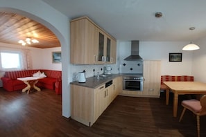 A compact kitchen with wooden cabinets, a built-in oven, and a dining area with a table and chairs. - Holiday apartment with 1 bedroom (Schönau am Königssee)