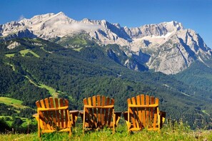 Three wooden Adirondack chairs facing a mountain range with a clear sky. - Holiday apartment with 2 bedrooms (Garmisch-Partenkirchen)