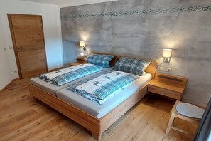 Een slaapkamer met een houten bed, twee nachtkastjes, een nachtkastje, een houten stoel en een deur.