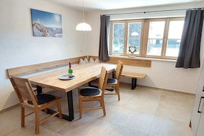 A dining area with a wooden table and chairs, a bench, a window with curtains, and a wall-mounted picture. - Holiday apartment with 2 bedrooms (Garmisch-Partenkirchen)