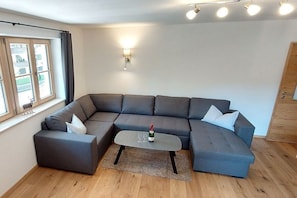 Een moderne woonkamer met een hoekbank, een klein bijzettafeltje en een raam met gordijnen.