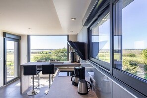 A modern kitchen with a large window, a coffee maker, and a dining area with two chairs. - Villa in Goulven with swimming pool (Goulven)