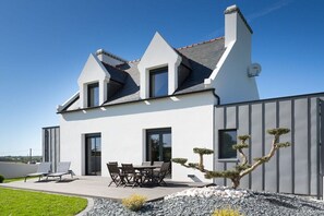 A modern two-story house with a patio, a dining area, and a bonsai tree. - Villa in Goulven with swimming pool (Goulven)