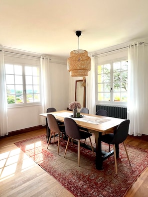 Un espace repas comprenant une table, des chaises, un luminaire suspendu et une vue dégagée sur l’extérieur grâce à de grandes fenêtres.