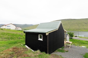 A small black wooden building with a sloped roof, a window, and a wooden bench outside.