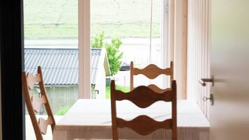 A dining area with a table and chairs, a view of a green landscape through a large window, and a wooden ceiling.