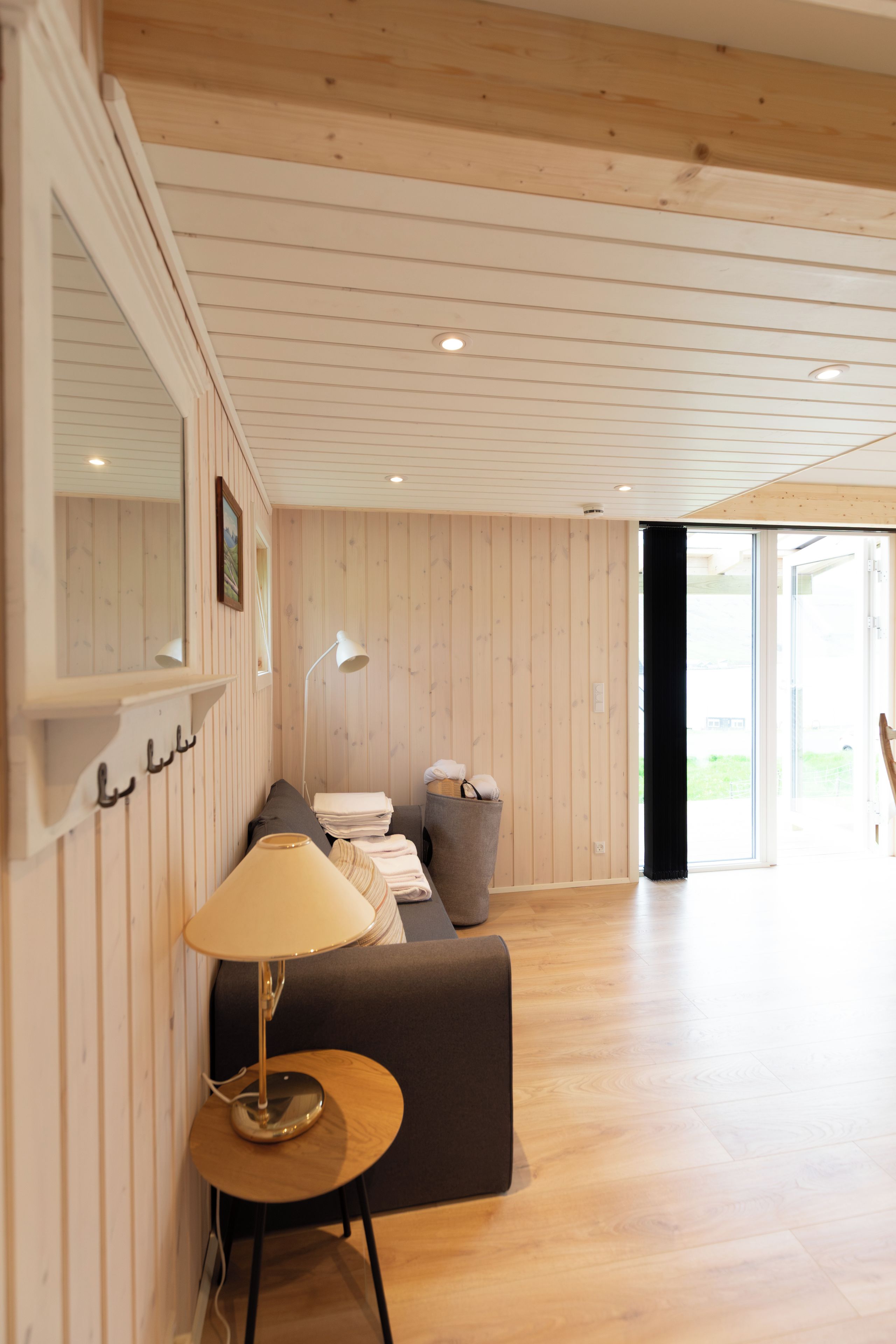 A room with a wooden ceiling, a sofa, a lamp, and a window.