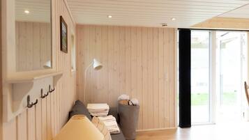A room with a wooden ceiling, a sofa, a lamp, and a window.