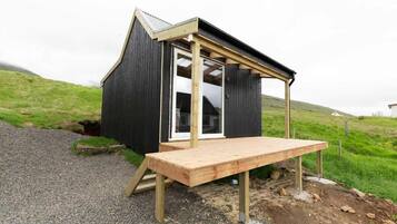 A small wooden structure with a sloped roof, a wooden deck, and a window.