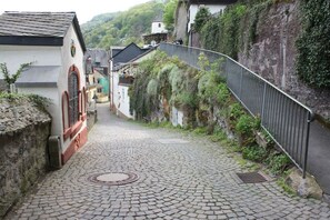 A cobblestone street in a village with buildings on either side, a metal fence, and a manhole cover in the center. - House Castle Romance (Cochem)
