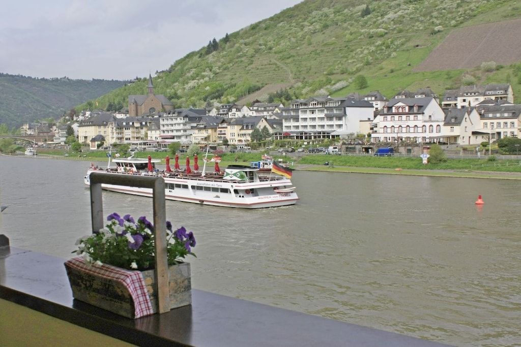 A river with a boat, buildings along the riverbank, and a hill in the background.