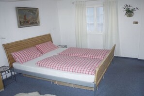 A double bed with checkered bedding, a bedside table, a lamp, a framed picture on the wall, and a window with curtains. - House Castle Romance (Cochem)
