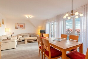 A modern living room with a dining area, a sofa set, a TV, and a large window with curtains. - Holiday apartment with 2 bedrooms (Norddeich)