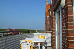 Un balcon avec une table et des chaises, un mur en briques et un ciel dégagé.
