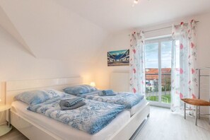 A bedroom with two beds, a window with curtains, a chair, and a painting on the wall. - Holiday apartment with 2 bedrooms (Norddeich)