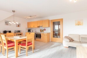 A modern kitchen with wooden cabinets, a dining table with chairs, and a white sofa in a bright room with a sloped ceiling. - Holiday apartment with 2 bedrooms (Norddeich)