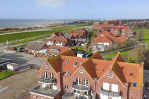 A coastal residential area with red-roofed houses, a beach in the background, and a clear sky. - Holiday apartment with 2 bedrooms (Norddeich)