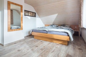 A bedroom with a sloped ceiling, a bed with a wooden frame, a mirror, and a small bedside table. - Holiday apartment with 2 bedrooms (Norderney)