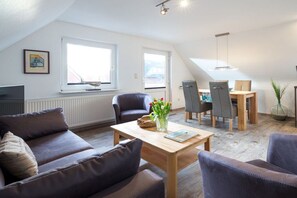 A modern living room with a sofa, a coffee table, and a dining area with chairs and a table. - Holiday apartment with 2 bedrooms (Norderney)
