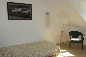 A small room with a single bed, a framed picture of horses, a standing lamp, and a chair. - Villa Les Brisants South Brittany (Loctudy)