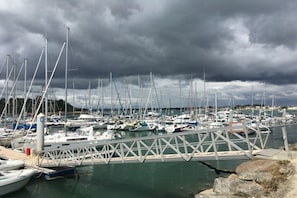 Un port de plaisance où sont amarrés de nombreux bateaux, un pont et un ciel nuageux.