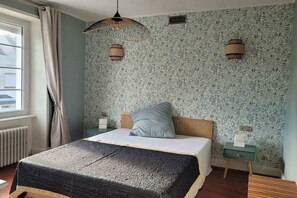 Une chambre à coucher avec un lit, une table de chevet, une lampe et une fenêtre avec des rideaux.