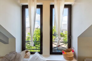 A room with a large window, a bed, a small table, and a basket with colorful items. - Cozy and bright loft in the town center by Groom* (Guidel)