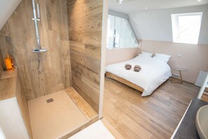 A modern bedroom with a wooden floor, a bed with white bedding, and a shower area. - Cozy and bright loft in the town center by Groom* (Guidel)