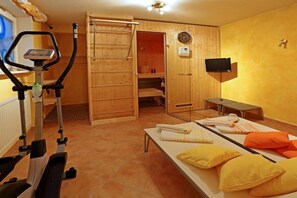 Une pièce équipée d’un tapis de course, d’une table de massage avec des serviettes et des oreillers, d’un téléviseur et d’une porte de sauna en bois.