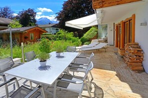 A patio with a table and chairs, a white umbrella, and a stack of firewood. - Holiday apartment with 1 bedroom (Garmisch-Partenkirchen)