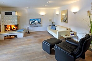 Un salon moderne avec une cheminée, un canapé, un fauteuil en cuir noir, un téléviseur et une petite table avec des livres.