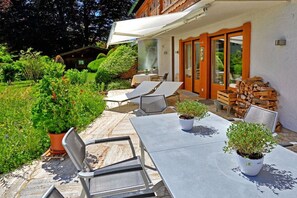 Eine Terrasse im Freien mit Tisch und Stühlen, einer überdachten Sitzgelegenheit und einem Holzstoß.