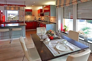 Uma cozinha moderna com armários vermelhos, uma ilha central e um espaço de refeições com mesa posta para dois.