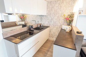 A modern kitchen with white cabinets, a black countertop, and a marble backsplash. - Beautiful Studio for 4 people with 180° sea view by Groom* (Ploemeur)
