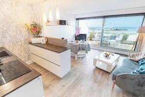 A modern kitchen with a dining area, a sofa, and a view of the sea. - Beautiful Studio for 4 people with 180° sea view by Groom* (Ploemeur)