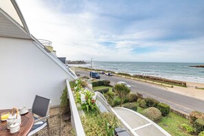 Un balcone con un tavolo apparecchiato per la colazione, vista su una strada costiera e una spiaggia.