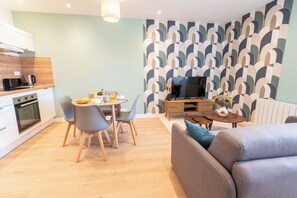 A modern living room with a dining area, a flat-screen TV, and a kitchen with a microwave and coffee maker. - Cozy and comfortable 2-bedroom duplex apartment by Groom* (Lorient)