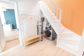 A laundry area with a washing machine, a drying rack, and a shelf. - Cozy and comfortable 2-bedroom duplex apartment by Groom* (Lorient)