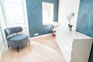 A room with a blue textured wall, a white cabinet, a grey chair, a small table with a lamp, and a potted orchid. - Cozy and comfortable 2-bedroom duplex apartment by Groom* (Lorient)