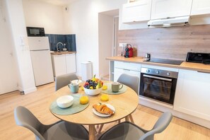 Et moderne køkken med hvide skabe, en mikrobølgeovn og en komfur. Der er et morgenbord med en skål frugt, en croissant og en kaffekop.