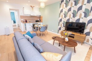 A modern living room with a sofa, coffee table, and TV. There's a dining area with chairs and a table. The room has wooden flooring and a patterned wall. - Cozy and comfortable 2-bedroom duplex apartment by Groom* (Lorient)