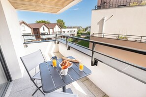 Ein Balkon mit Frühstückstisch, ausgestattet mit Croissants und Orangensaft, mit Blick auf eine Wohngegend.
