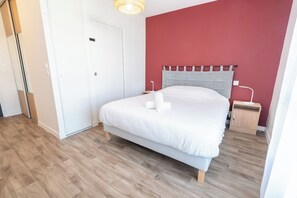 Ein Schlafzimmer mit Bett, Nachttisch, Tür und einer Wand mit rotem Akzent.