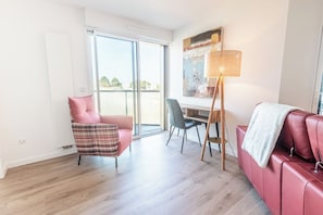 Ein modernes Wohnzimmer mit einem roten Sofa, einem karierten Sessel, einem Esstisch mit Stühlen und einer Stehlampe.